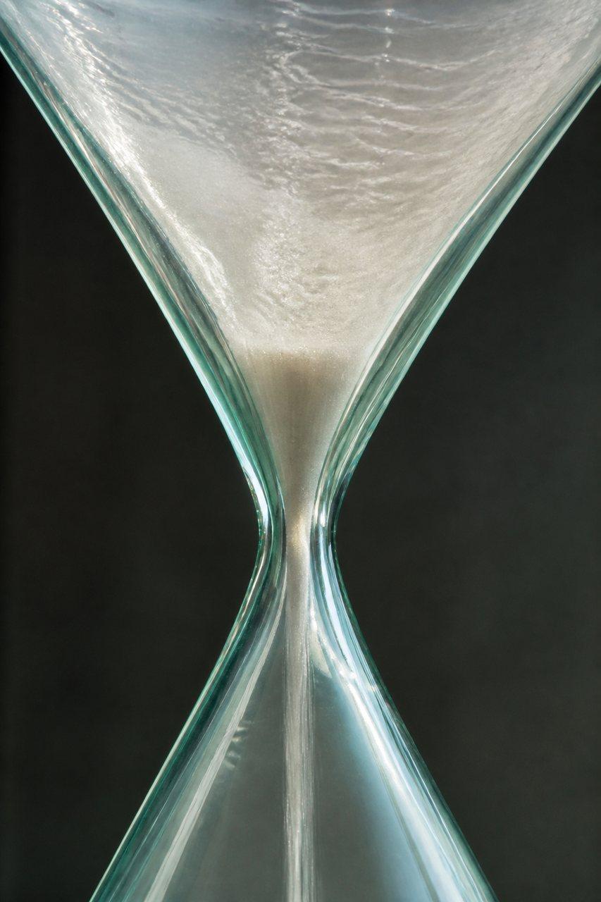 Sand concentrating through the narrow waist of a glass hourglass